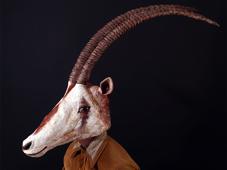 A figure of a man wears a mask that resembles a gazelle with long curved antlers..