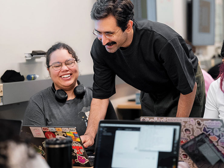 A Muhlenberg faculty members leans over a student's laptop in a classroom.
