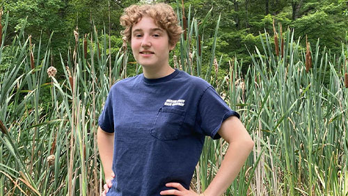 A college students stands outdoors in a wetlands.
