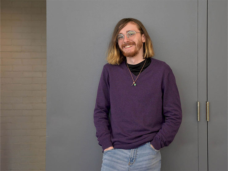 College student Eamon Bonner stands against a wall, smiling with hands in pockets.