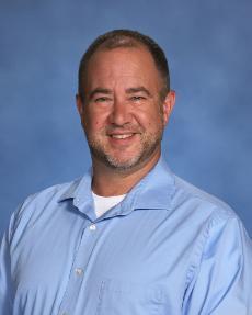 Faculty member Jim Tully seated for portrait wearing blue collared shirt.