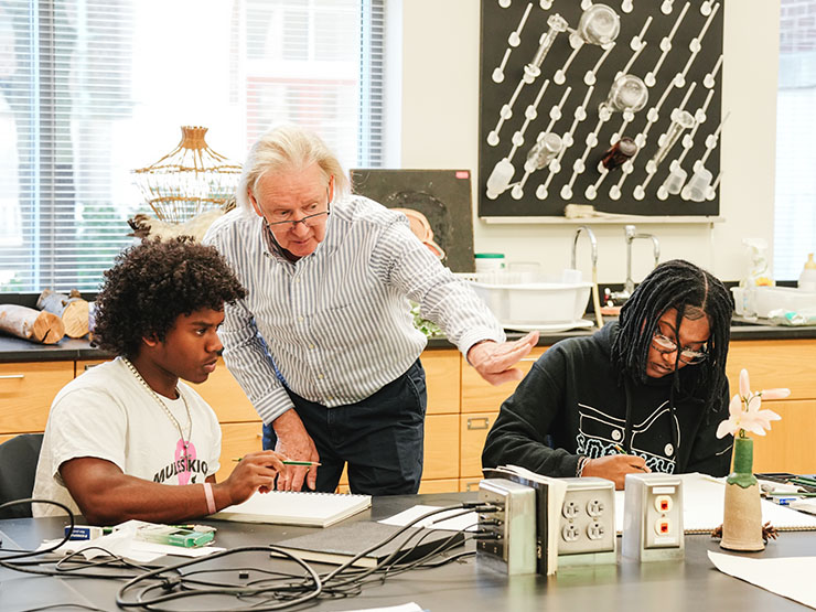 A professor providing instruction to two students in classroom setting.