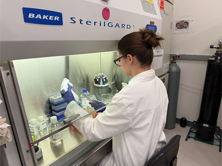 A college student in a lab coat performs research in a lab.