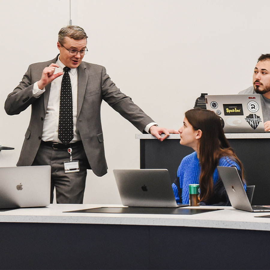 Greg Collins, a college professor dressed in a suit, speaks to a classroom of students.
