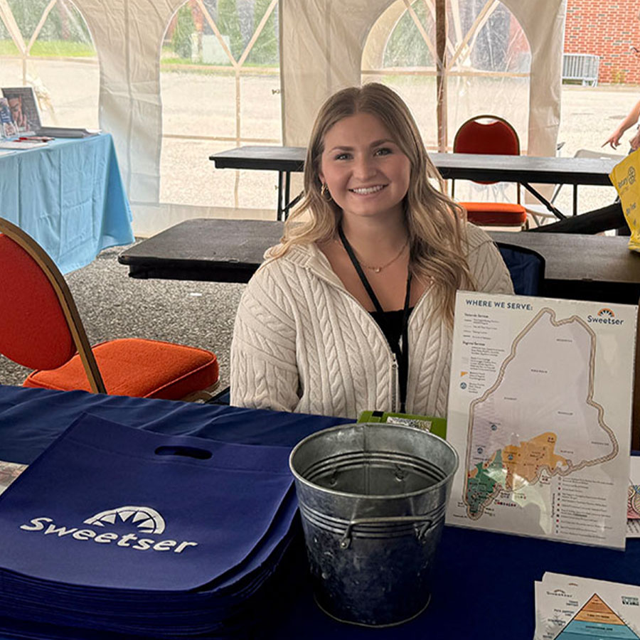 College student Greta Marchildon smiles while seated behind a table at mental health awareness event.