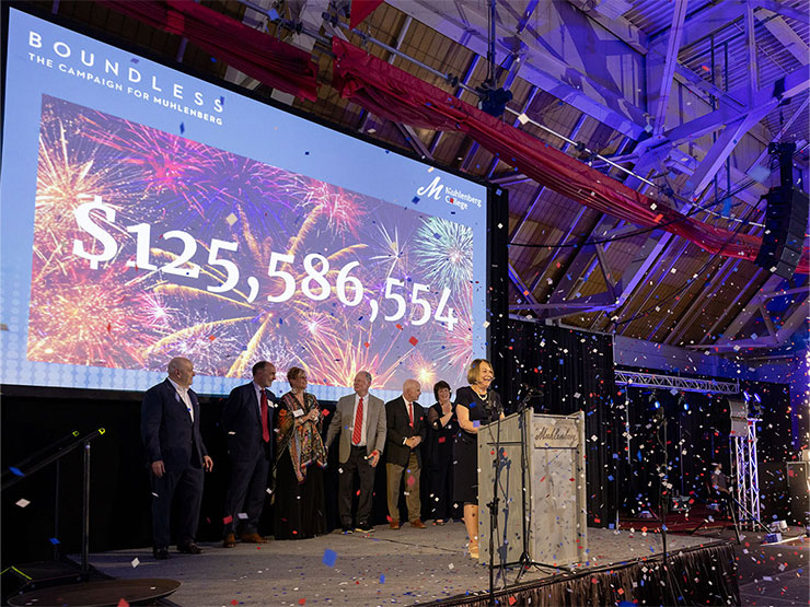 College President Kathleen Harring and others stand on stage showered in confetti with large dollar amount projected on screen behind them.
