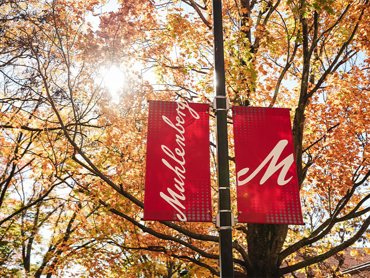 Red Muhlenberg College banners stand against orange and yellow autumn foaliage.