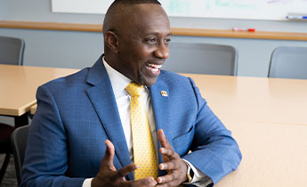 An adult in a suit smiles while chatting at a table in a classroom.