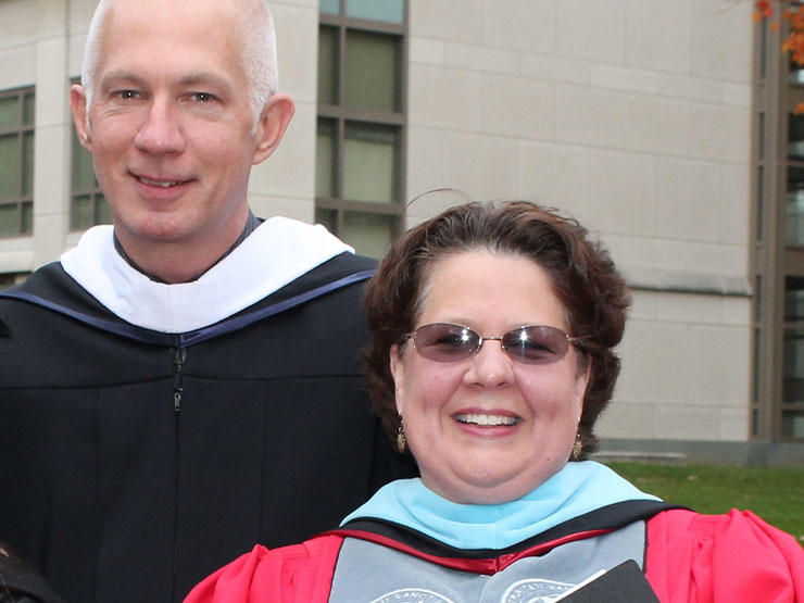A pair of adults in graduation regalia smile at the camera.