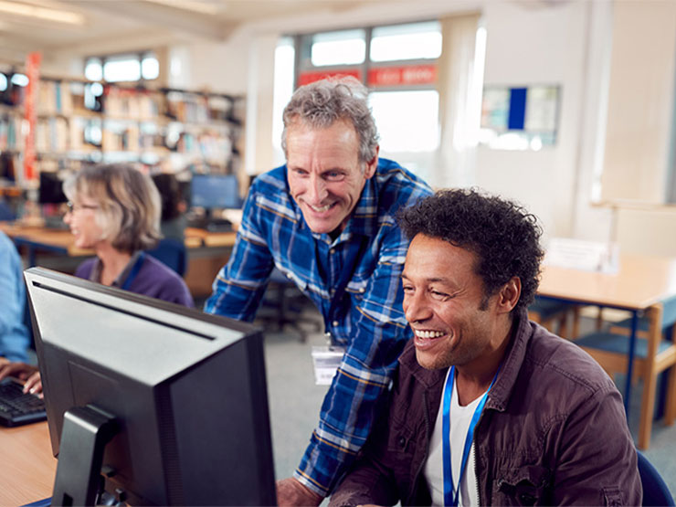 Student and mentor in discussion at computer desk in library setting.