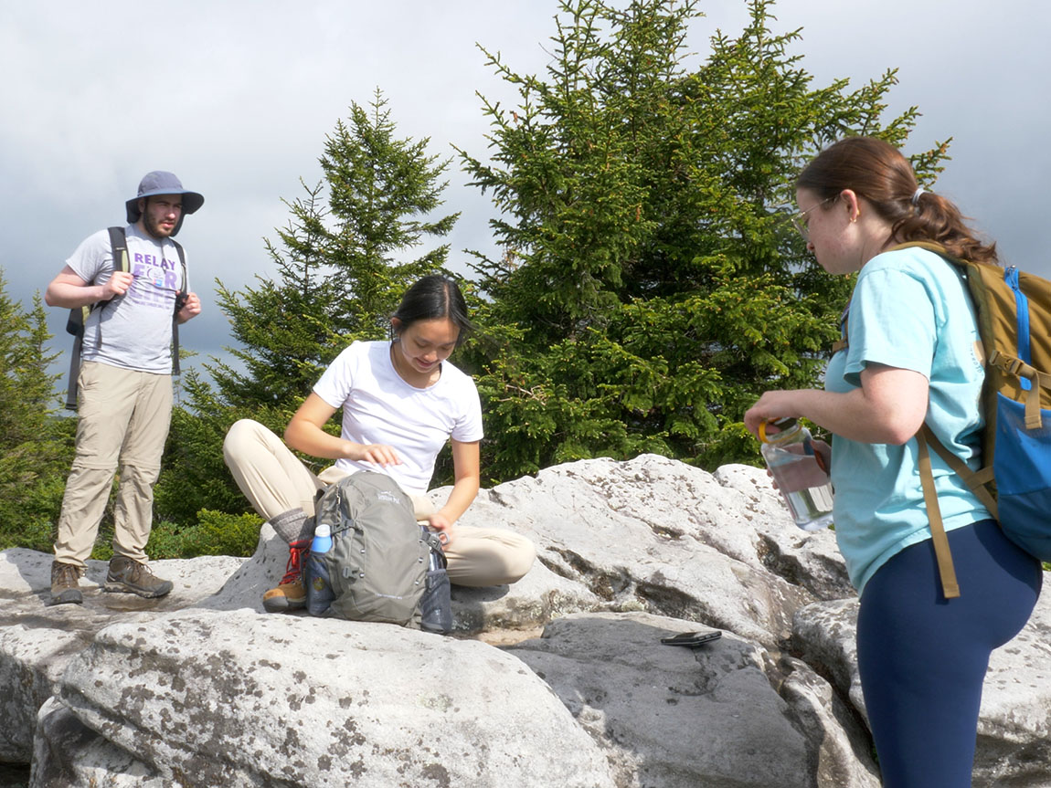 Three college students hike on a rocky hill
