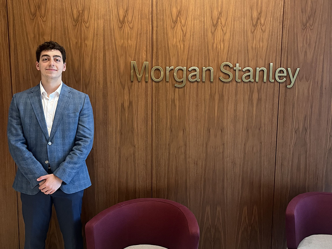 A college student in a suit next to a sign that says Morgan Stanley