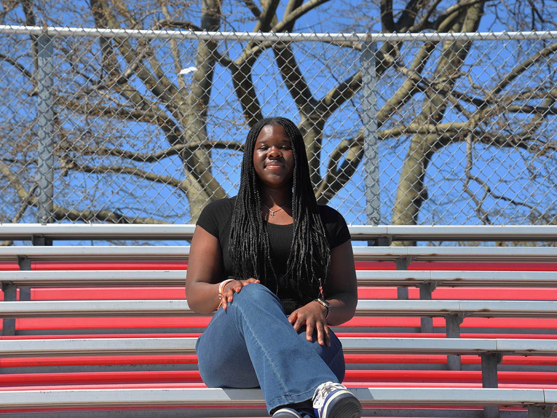 A college student sits with crossed legs on some bleachers outside