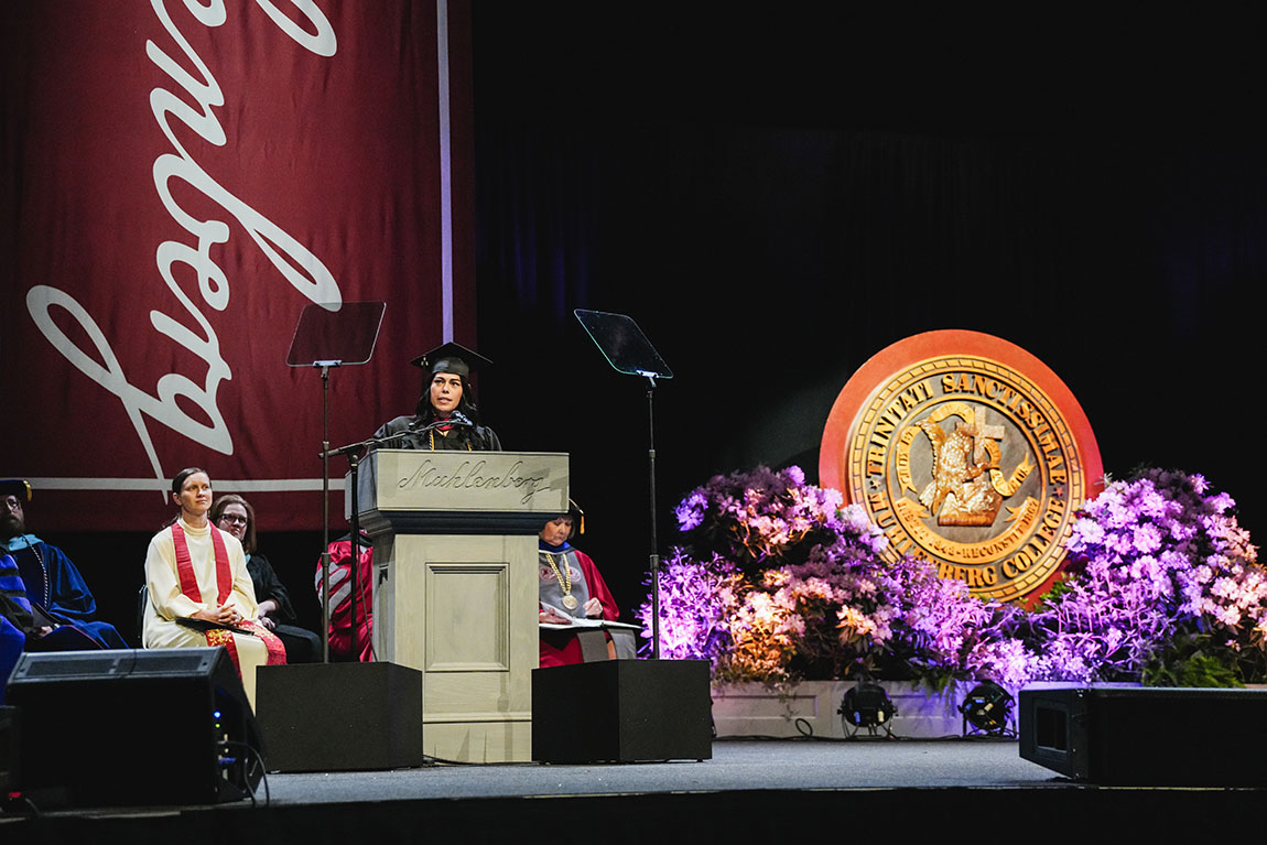 A college students in cap and gown delivers a commencement address on stage