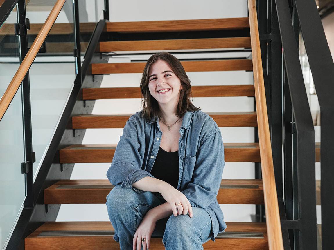 A college student sits on wooden steps inside a building