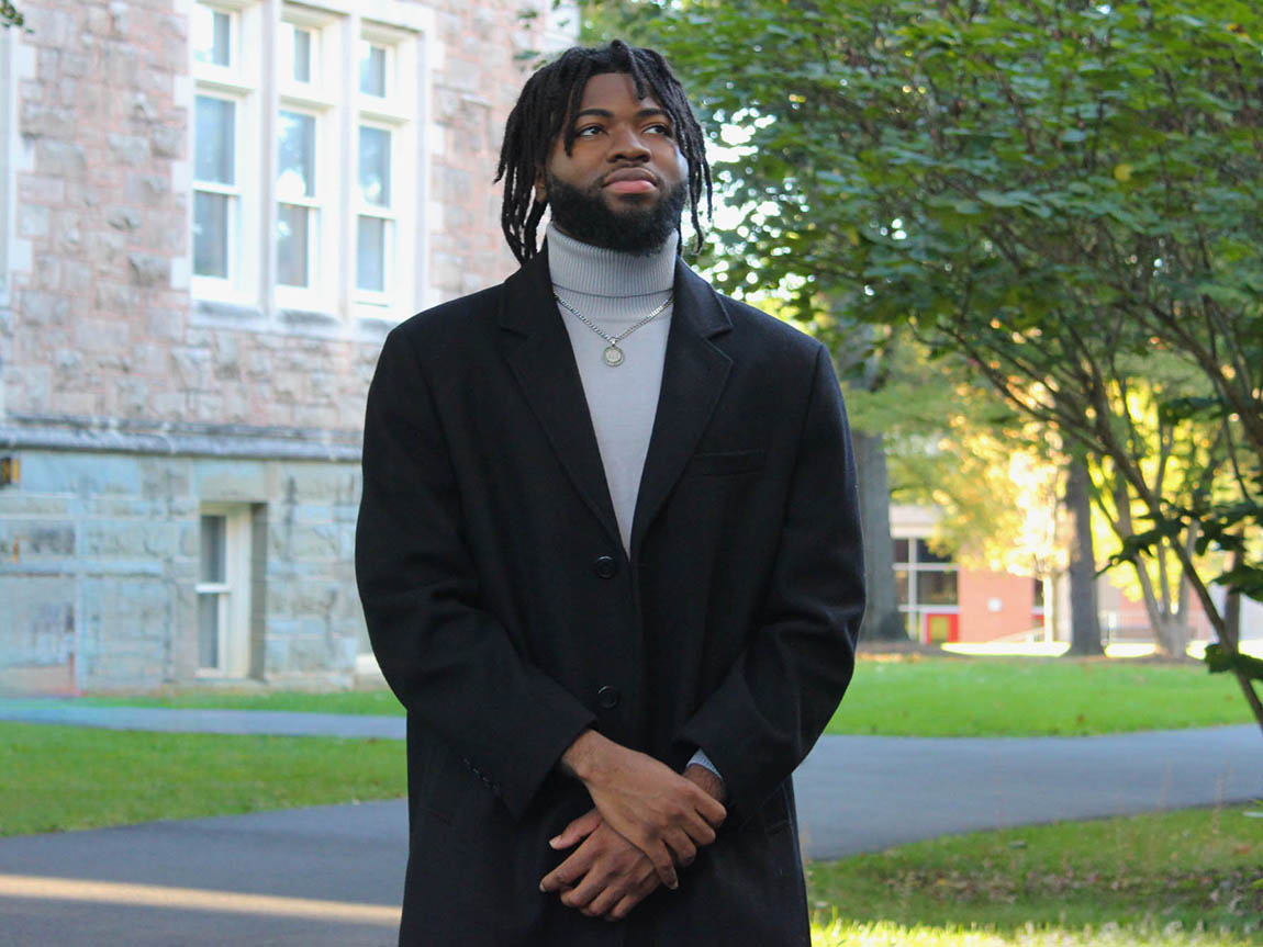 A college student stands outside in a blazer and turtleneck