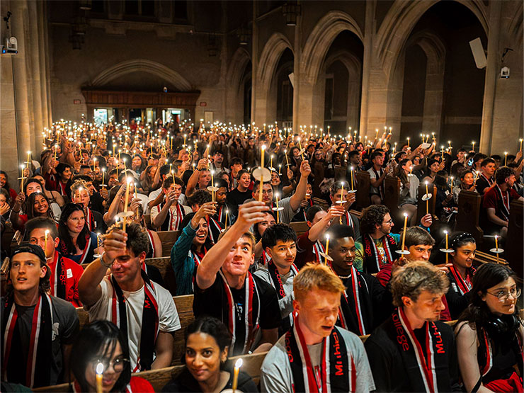 The inside of a chapel is packed with college student holding candles and wearing Muhlenberg scarfs.