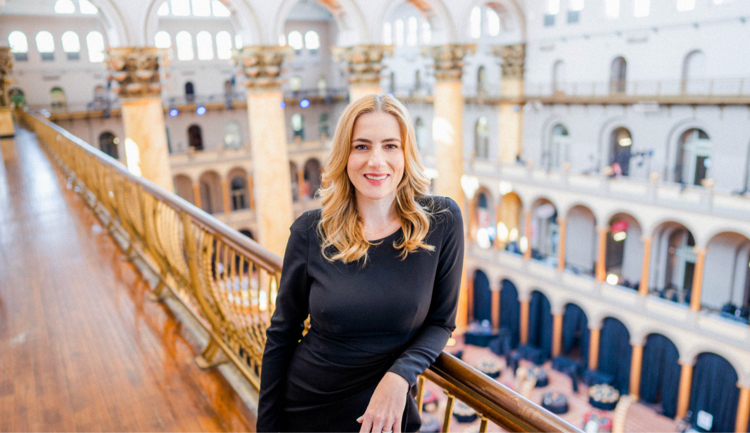 A woman stands leaning on an outdoor balcony railing.