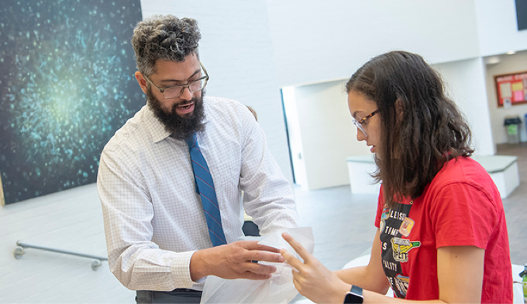 A professor in conversation with a student inside a college building foyer.