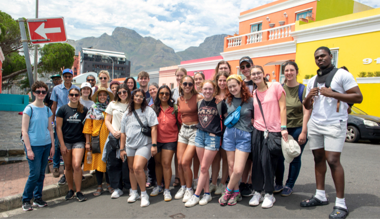 A group of people traveling pose together for a photograph outdoors.