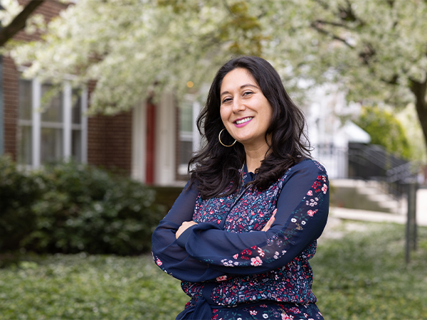 A female instructor stands outside of a college officer with her arms crossed.